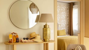 A hotel room with a round mirror, a table with a lamp, a bed with a yellow bedspread, and a chair with a striped bag. - Villa Léa, l’écrin du Fer à Cheval (Trouville-sur-Mer)