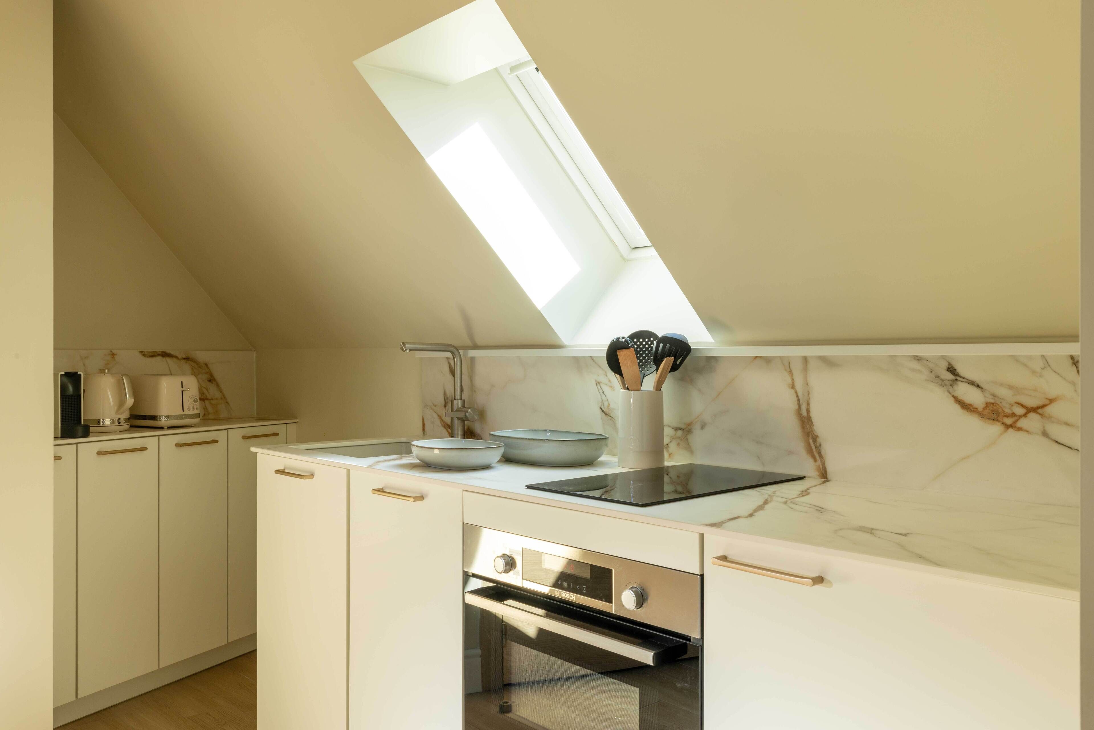 Eine Küche mit Oberlicht, weißen Schränken, einem eingebauten Backofen und einer Marmor-Spritzschutzwand.