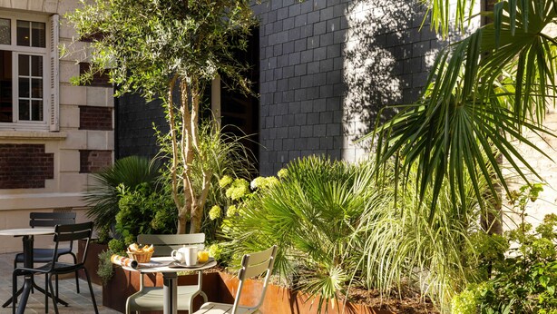A patio with a table and chairs, surrounded by various plants and a brick wall. - Villa Léa, l’écrin du Fer à Cheval (Trouville-sur-Mer)