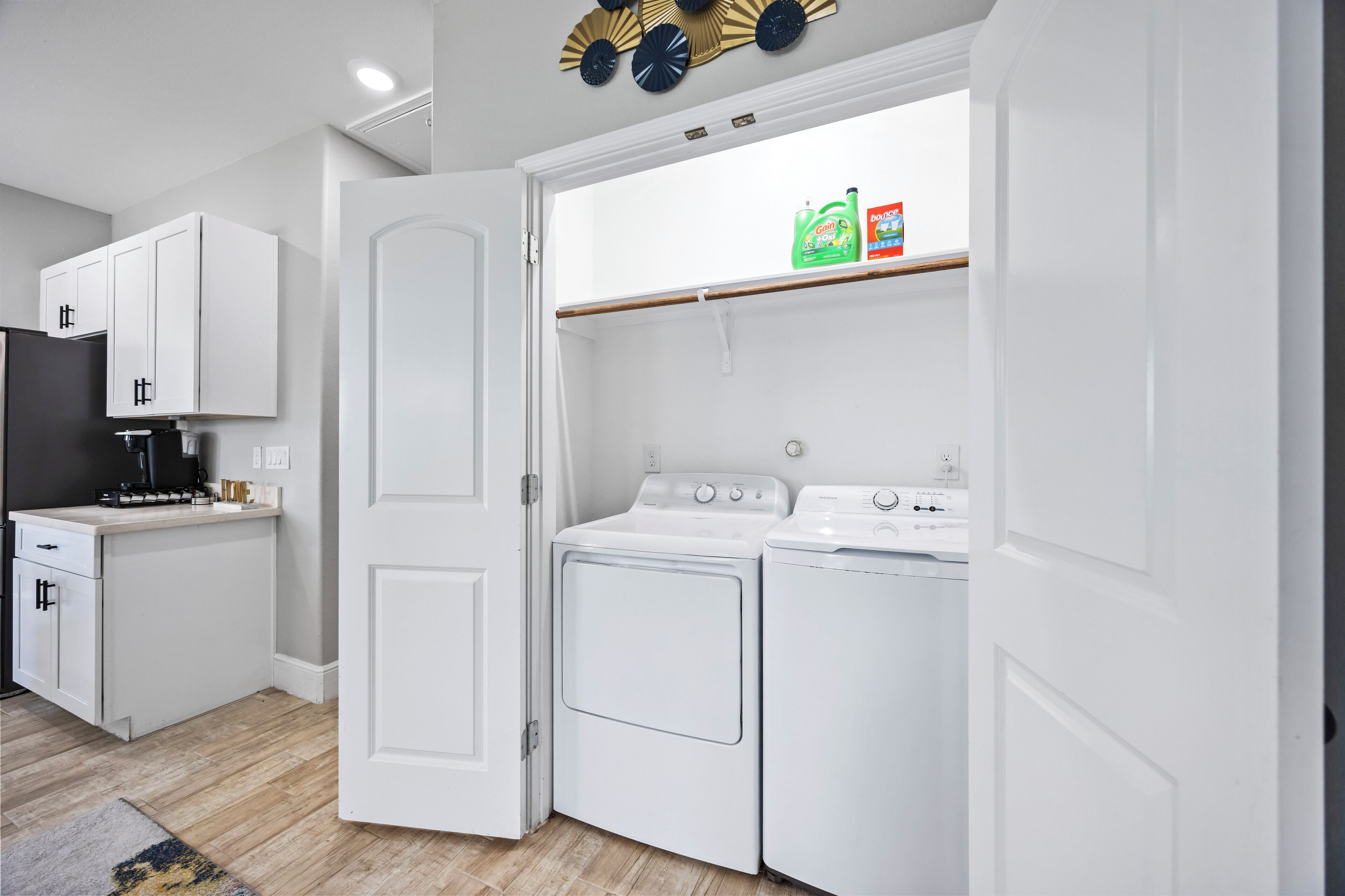 A compact laundry room with a washing machine and dryer, a coffee maker, and a shelf with cleaning products.