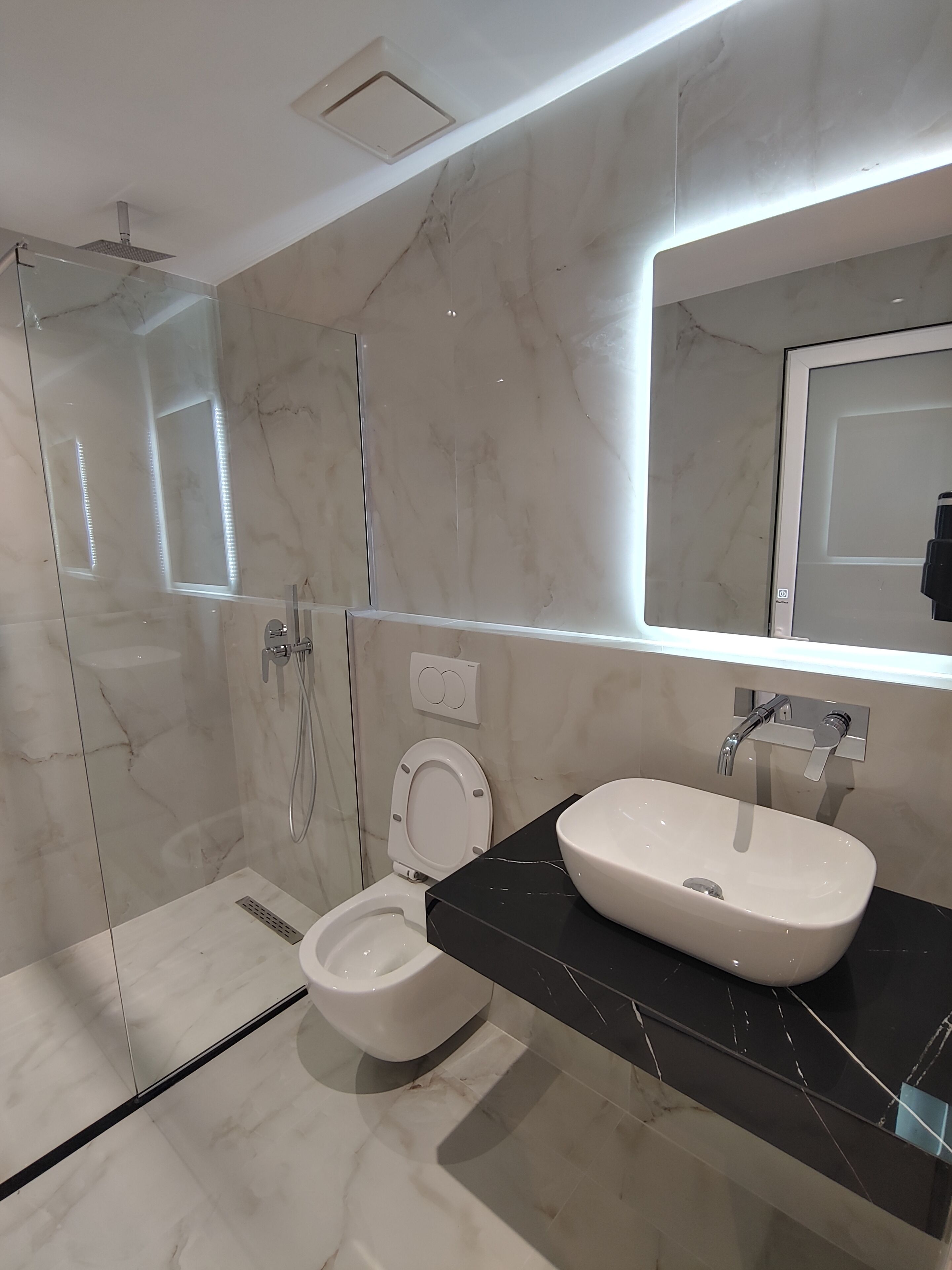 A modern bathroom with a glass-enclosed shower, a toilet, and a sink with a mirror above it.