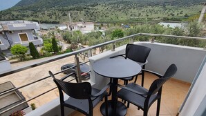 Un balcon avec une table et des chaises, une vue sur un paysage vallonné et un bâtiment en arrière-plan.