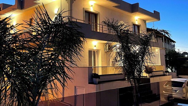 Une maison moderne à deux étages, dotée d’un balcon, avec une voiture garée devant et un ciel dégagé.
