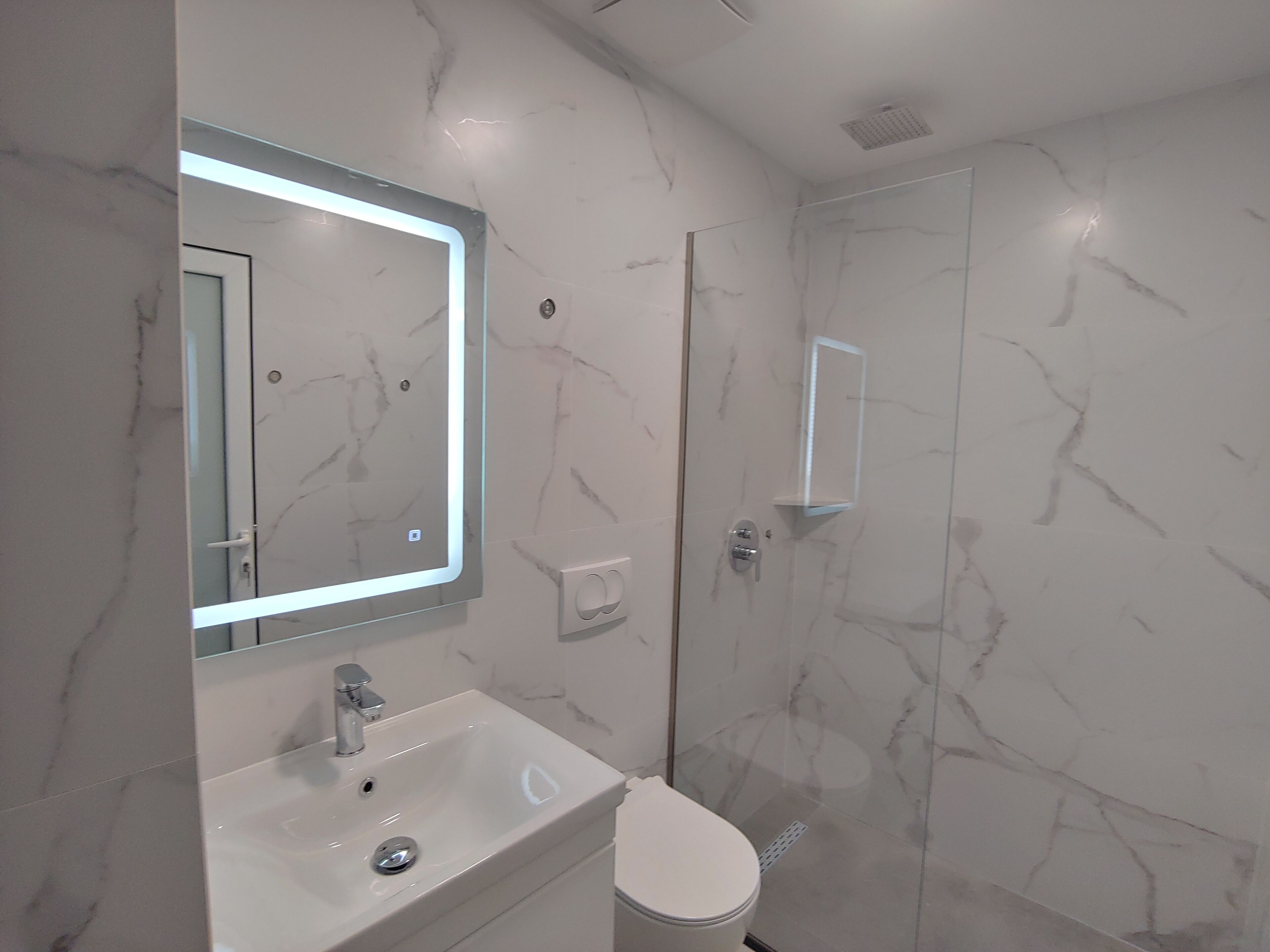 Une salle de bain moderne avec un pare-baignoire en marbre, un lavabo intégré, un miroir et des toilettes.
