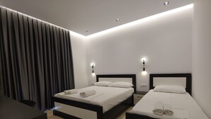 Une chambre d’hôtel moderne avec deux lits, une grande fenêtre avec des rideaux et un éclairage encastré au plafond.