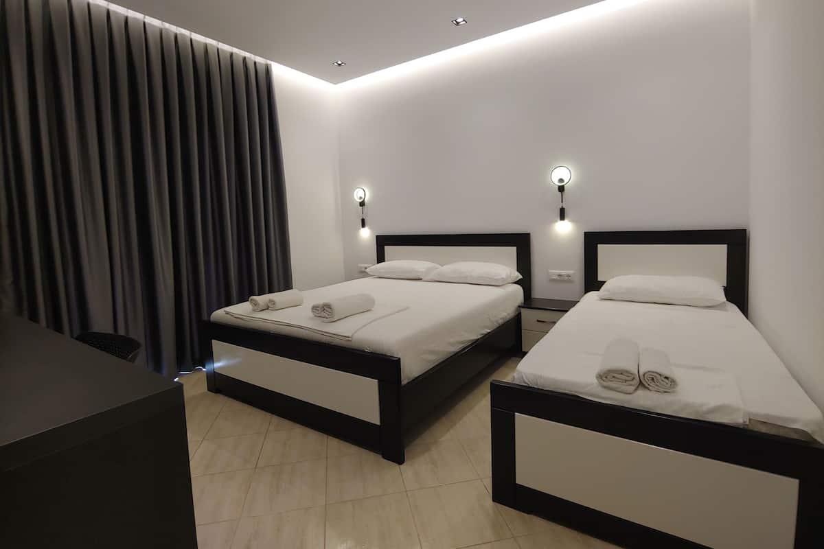 A modern hotel room with two beds, a large window with curtains, and recessed ceiling lighting.