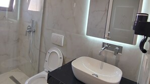 Une salle de bain moderne avec une douche à parois de verre, des toilettes blanches, un plan de toilette noir et un grand miroir.