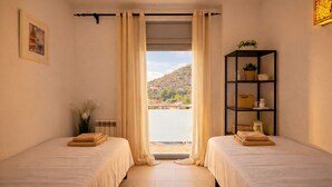 A room with two beds, a window with curtains, a radiator, a framed picture, and a shelf with items. - Duplex in Sitges with sea views, parking, terrace, balcony (Sitges)