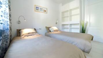 A bedroom with two beds, a wall-mounted shelf unit, and a window with blinds.
