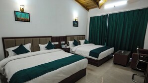 Una habitación de hotel con dos camas, una mesita, una silla y un ventanal con cortinas.