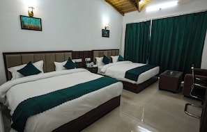 Quarto de hotel com duas camas, uma mesa pequena, uma cadeira e uma janela com cortinas.