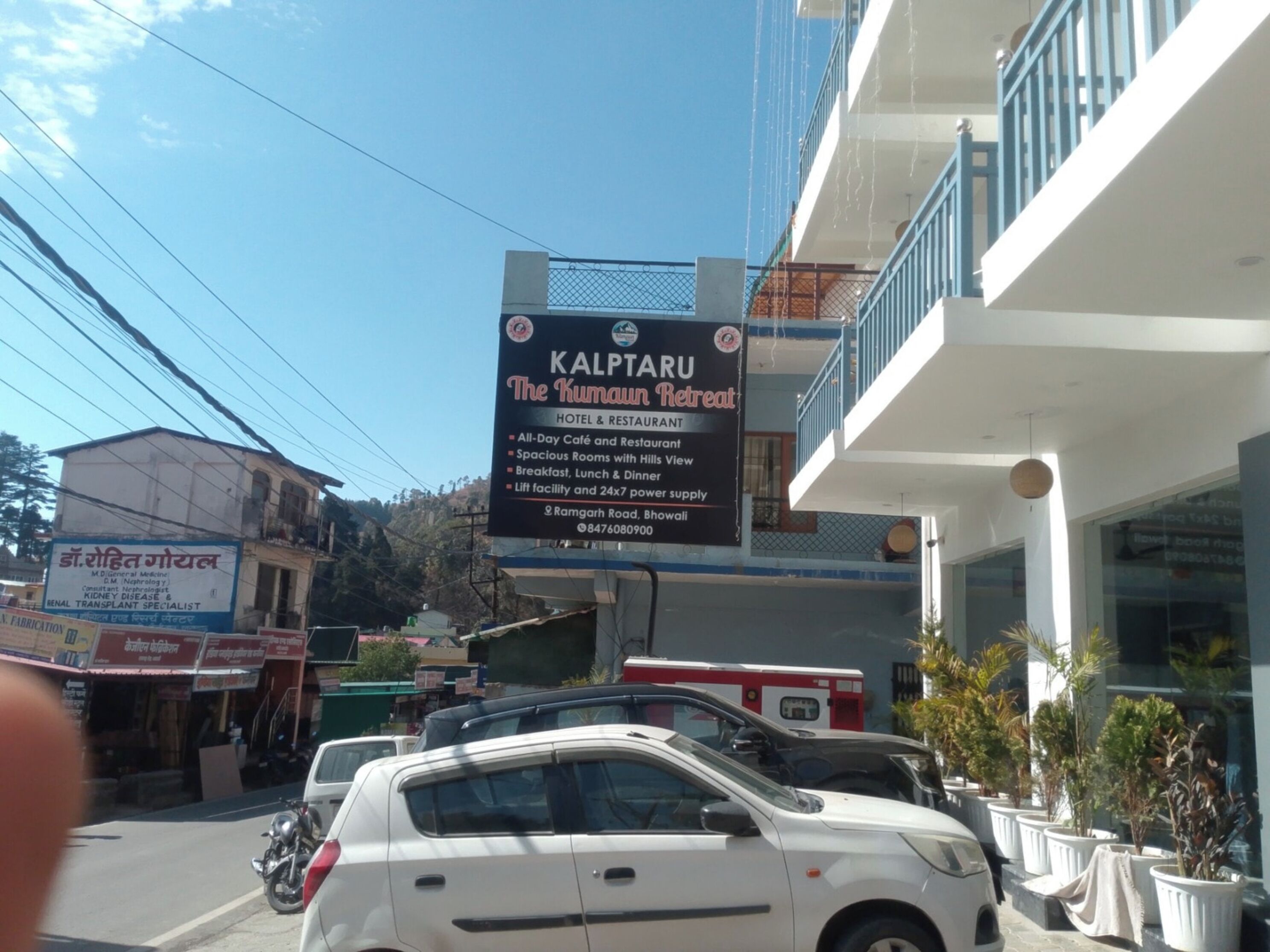 A signboard for 'Kalpataru The Kumau Retreat' hotel and restaurant, listing amenities like a 24x7 power supply and breakfast.