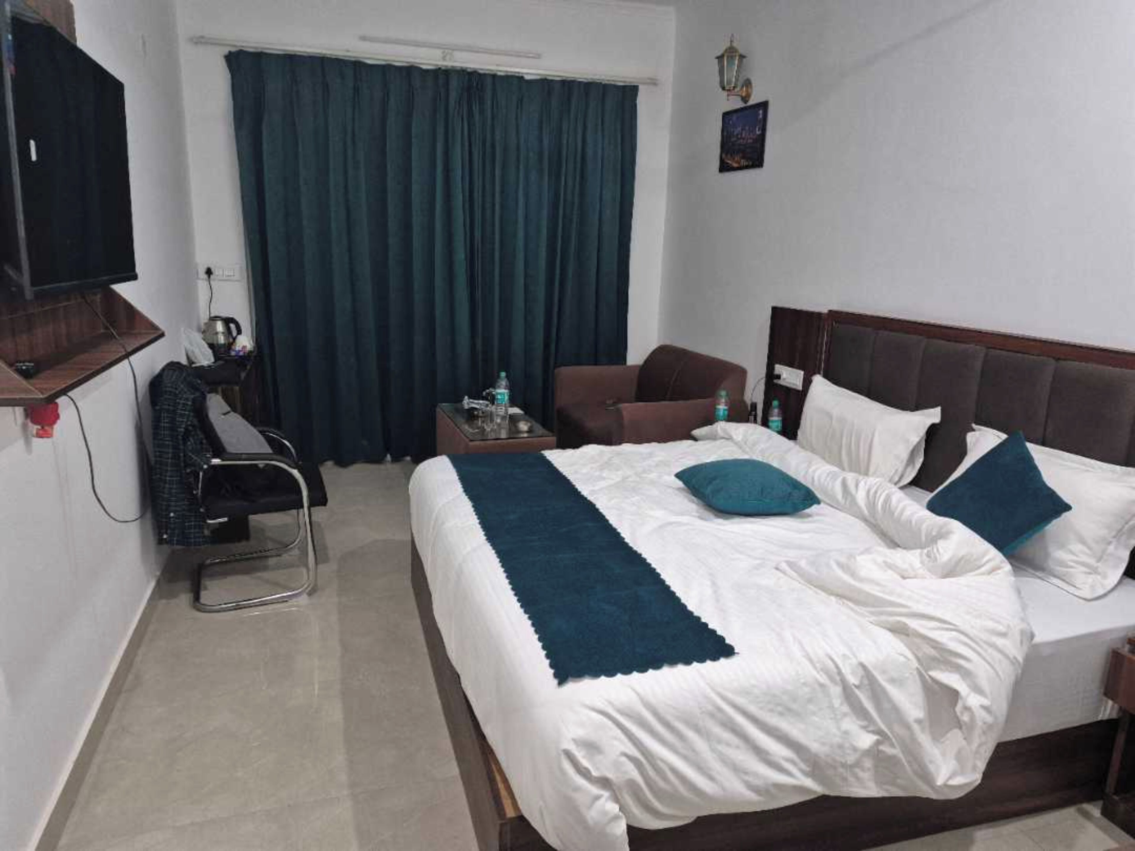 A hotel room with a bed, a chair, a desk, a TV, and a window with curtains.