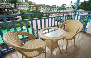Un balcon doté de fauteuils en osier et d’une table en verre, offrant une vue sur un quartier résidentiel avec ses immeubles et sa verdure.