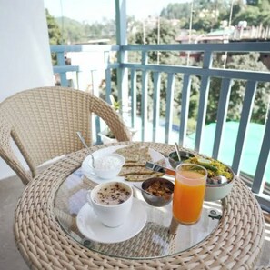 A wicker chair and table with a meal and drink on a balcony overlooking a body of water.