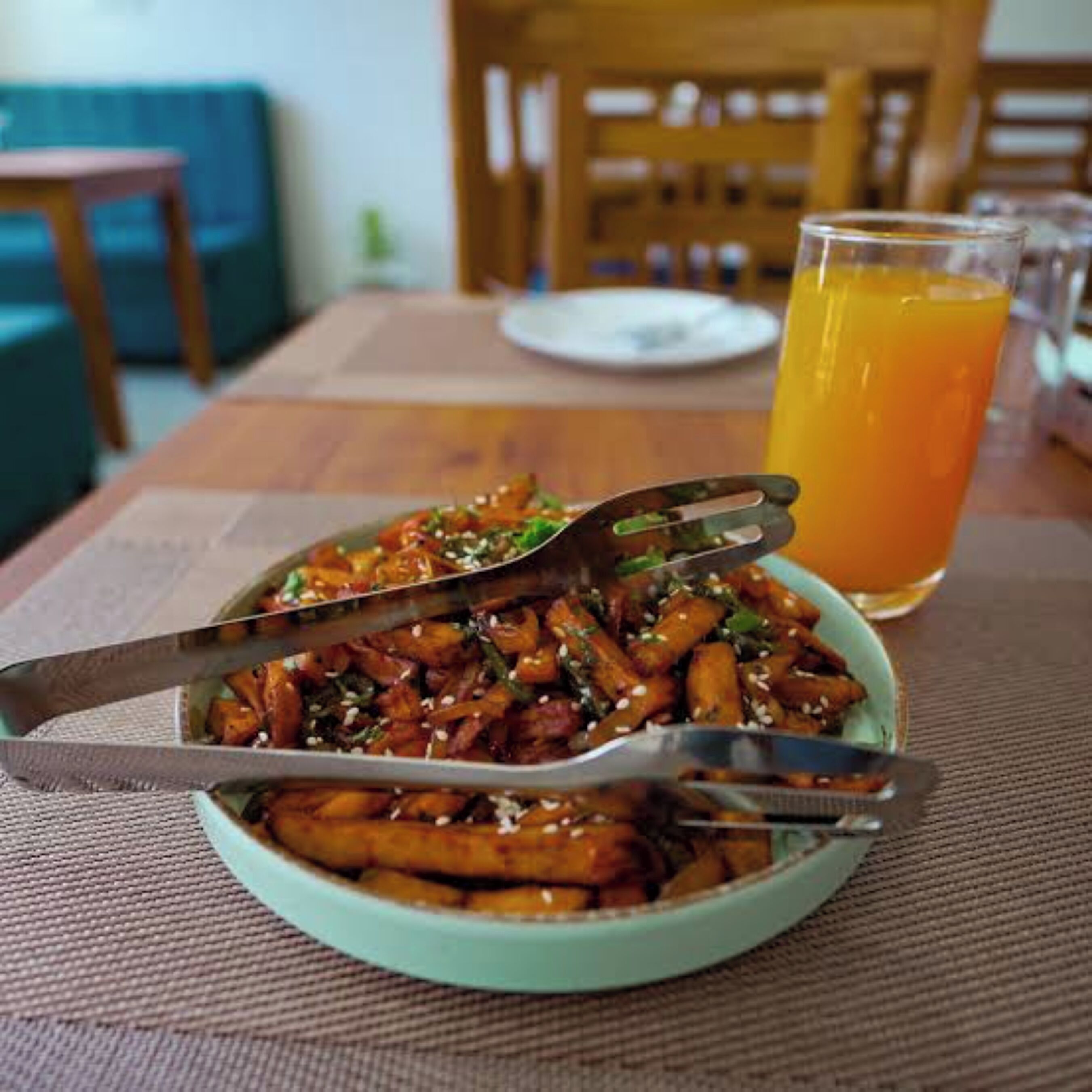 Un bol de légumes sautés, une pince à servir, un verre de jus d’orange et une table à manger.