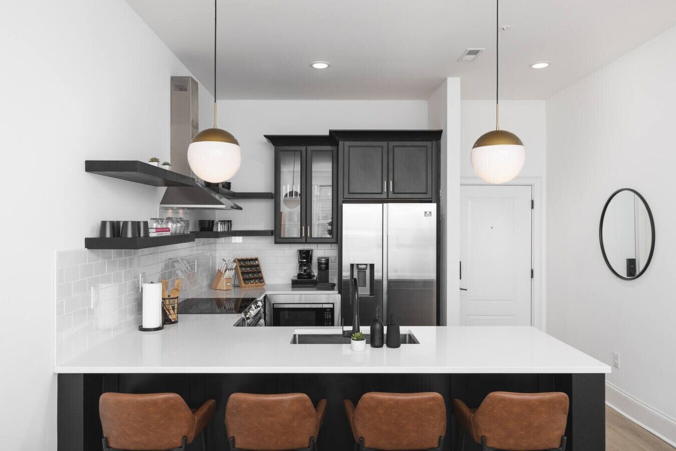A modern kitchen with a central island, black cabinets, stainless steel appliances, and pendant lighting.