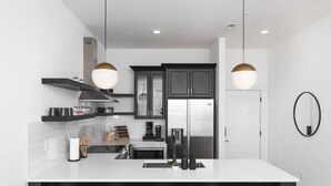 Una cucina moderna con isola centrale, mobili neri, elettrodomestici in acciaio inossidabile e illuminazione a sospensione.