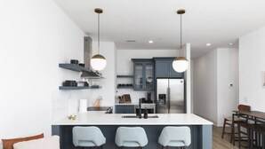 A modern kitchen with a central island, bar stools, and a dining area with a wooden table and chairs.