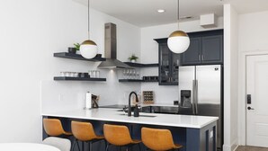 A modern kitchen with a central island, bar stools, stainless steel appliances, and pendant lighting.