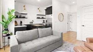 A modern apartment with a grey sofa, a kitchen with white cabinets, and a dining area. - Sleeps 32, only 10 minutes to Broadway, 4 Condos Side-by-Side (Nashville)
