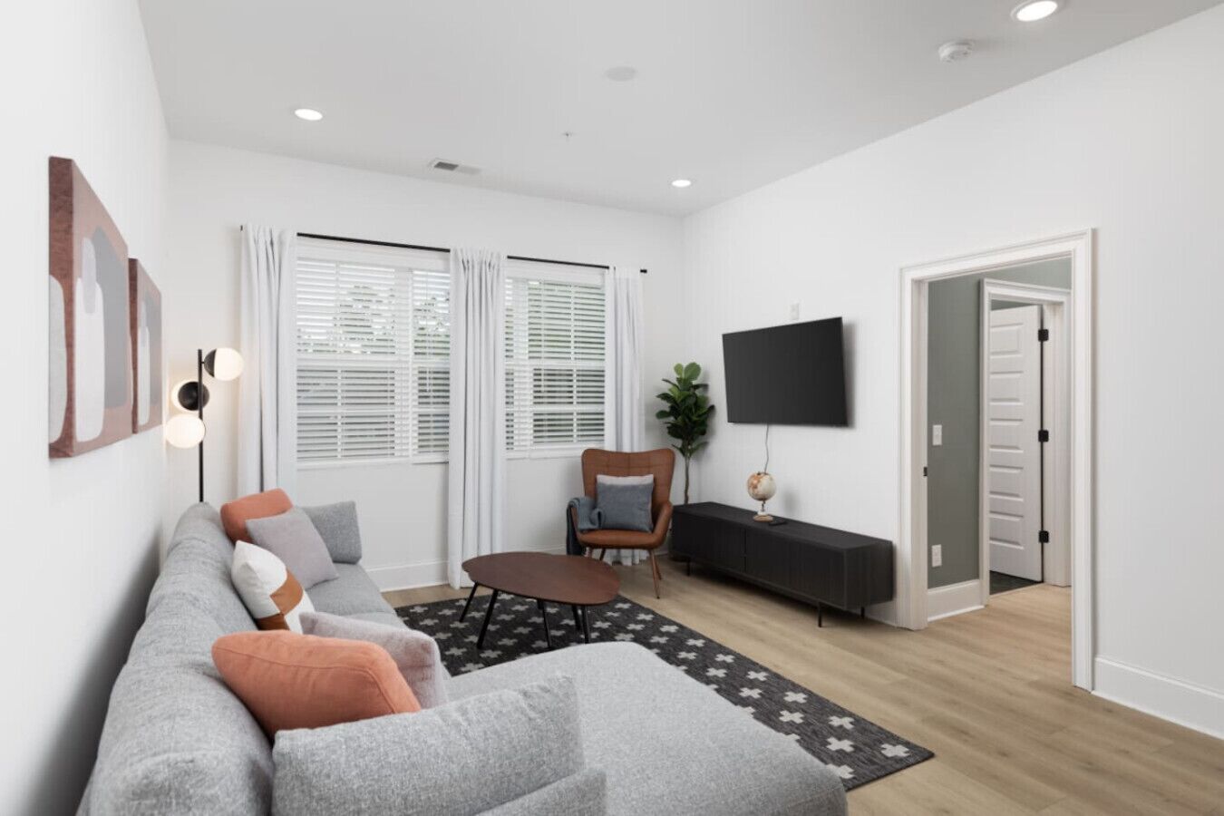 Un salon moderne avec un canapé gris, une petite table basse ronde et un téléviseur fixé au mur.