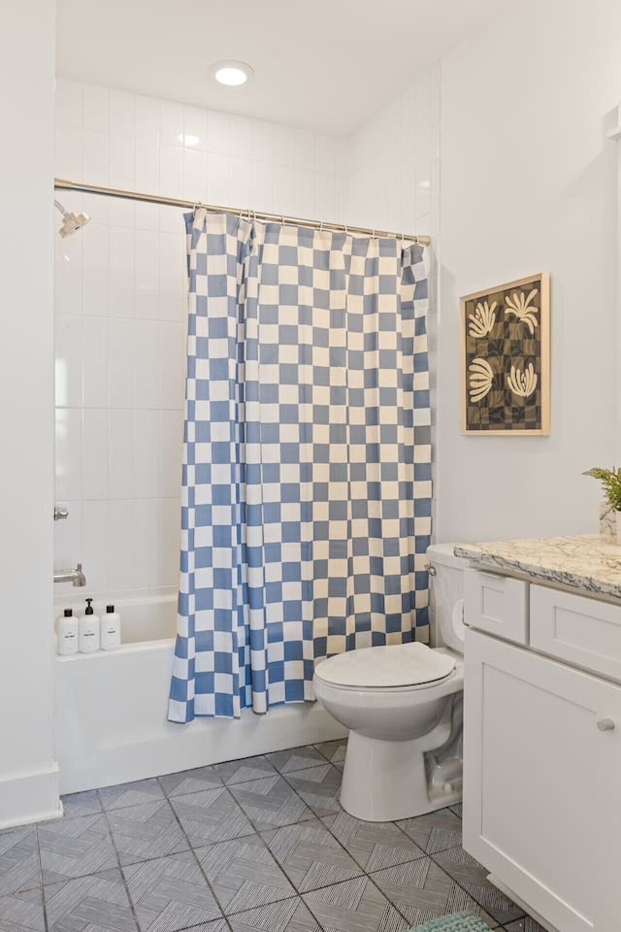 Une salle de bain avec un rideau de douche à carreaux, des toilettes, un lavabo doté d’un plan de travail en marbre et une œuvre d’art accrochée au mur.