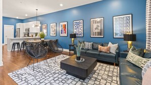 Een moderne woonkamer met een blauwe accentmuur, een eethoek en een witte keuken op de achtergrond, plus een plafondventilator.