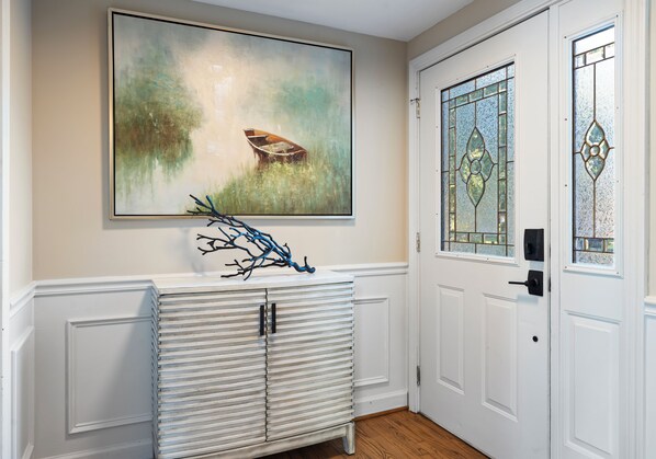 Un couloir avec une porte blanche, un meuble blanc fixé au mur et un grand tableau abstrait au-dessus du meuble.
