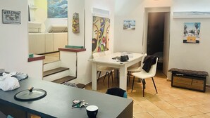 Una sala moderna con comedor, sofá, mesa de centro y televisor. Hay obras de arte en las paredes y un cartel de bienvenida.