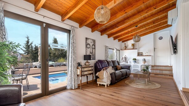 A spacious living area with a wooden ceiling, a leather sofa, a coffee table, and a view of a swimming pool. - Es Refugi de les Aguiles (Lloseta)