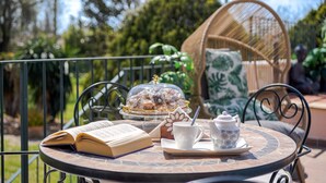 An outdoor dining area with a round table, a wicker chair, a covered dessert display, a book, and a teapot. - Es Refugi de les Aguiles (Lloseta)