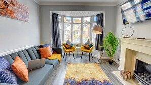 A modern living room with a grey sofa, yellow armchairs, a fireplace, and a large window with curtains. - 4 BedRoom House | w/ FREE Wi-fi | Parking (West Midlands)