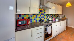 A kitchen with white cabinets, a colorful backsplash, a red microwave, a gas stove, and a hanging light fixture. - 4 BedRoom House | w/ FREE Wi-fi | Parking (West Midlands)