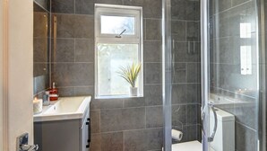 A modern bathroom with a glass shower enclosure, a white sink, and a window providing natural light. - 4 BedRoom House | w/ FREE Wi-fi | Parking (West Midlands)