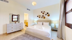 Hotelkamer met een groot bed, een kaptafel met gouden handgrepen, een flatscreen televisie, een decoratief object aan de muur en een raam met gordijnen.