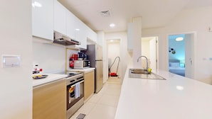 Een moderne keuken met een centraal eiland, een inbouwoven en een magnetron. Er is een spoelbak met een kraan en een stofzuiger op de achtergrond.