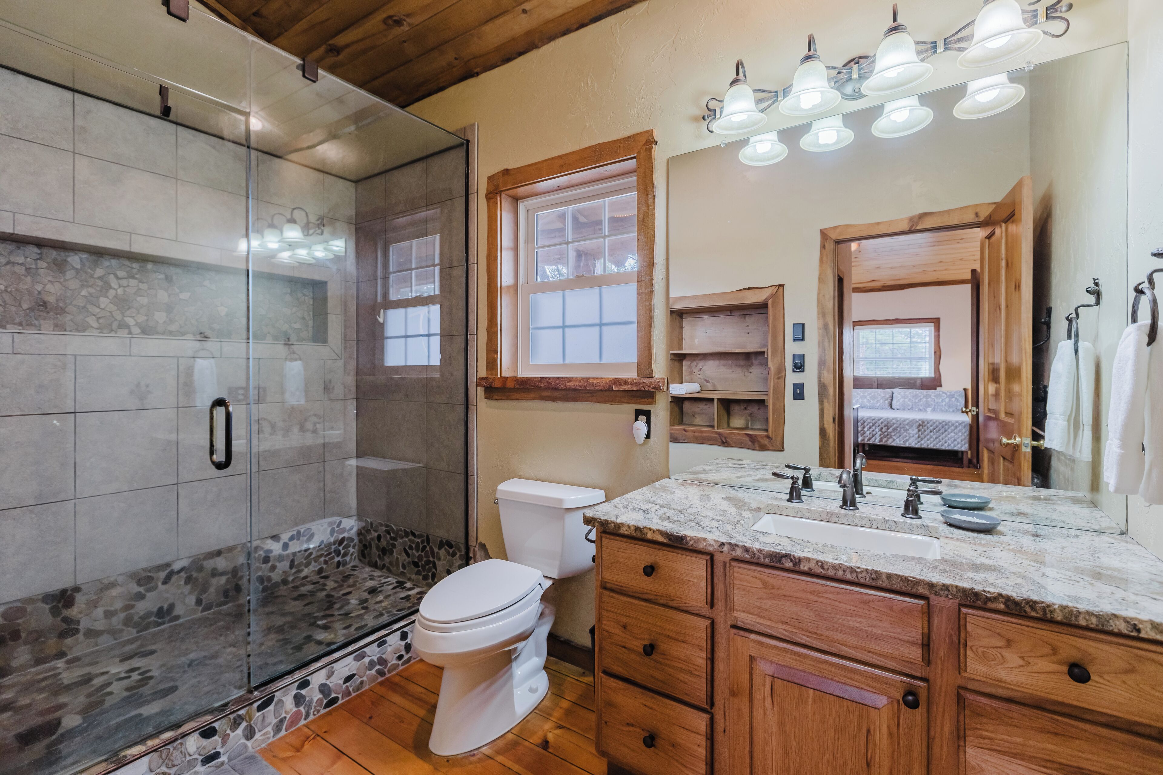 A bathroom with a glass-enclosed shower, a white toilet, wooden cabinets, and a marble countertop.