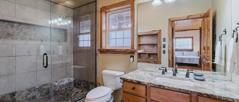 A bathroom with a glass-enclosed shower, a white toilet, wooden cabinets, and a marble countertop.