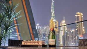 Une bouteille de champagne Moët & Chandon, deux verres vides et un dessert sur une table, avec une vue sur le paysage urbain en arrière-plan.