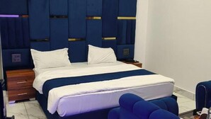Ein ordentlich bezogenes Bett mit weißer und blauer Bettwäsche, ein Nachttisch aus Holz mit einer Lampe und ein blauer Sessel.