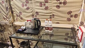 A small kitchenette with a glass-top table, a refrigerator, and a patterned curtain in the background.