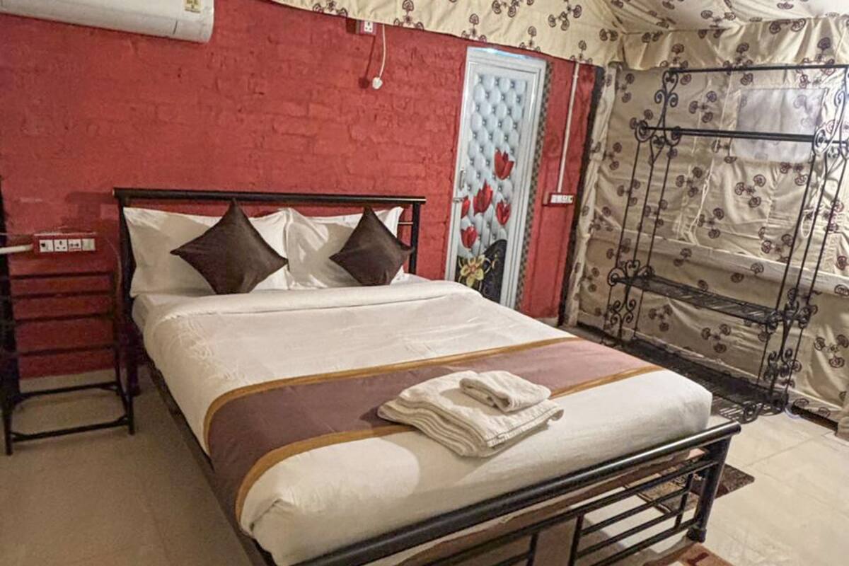 Un lit avec un cadre en métal, un rideau à motifs et un mur rouge.