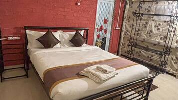 Una cama con estructura metálica, una cortina estampada y una pared roja.
