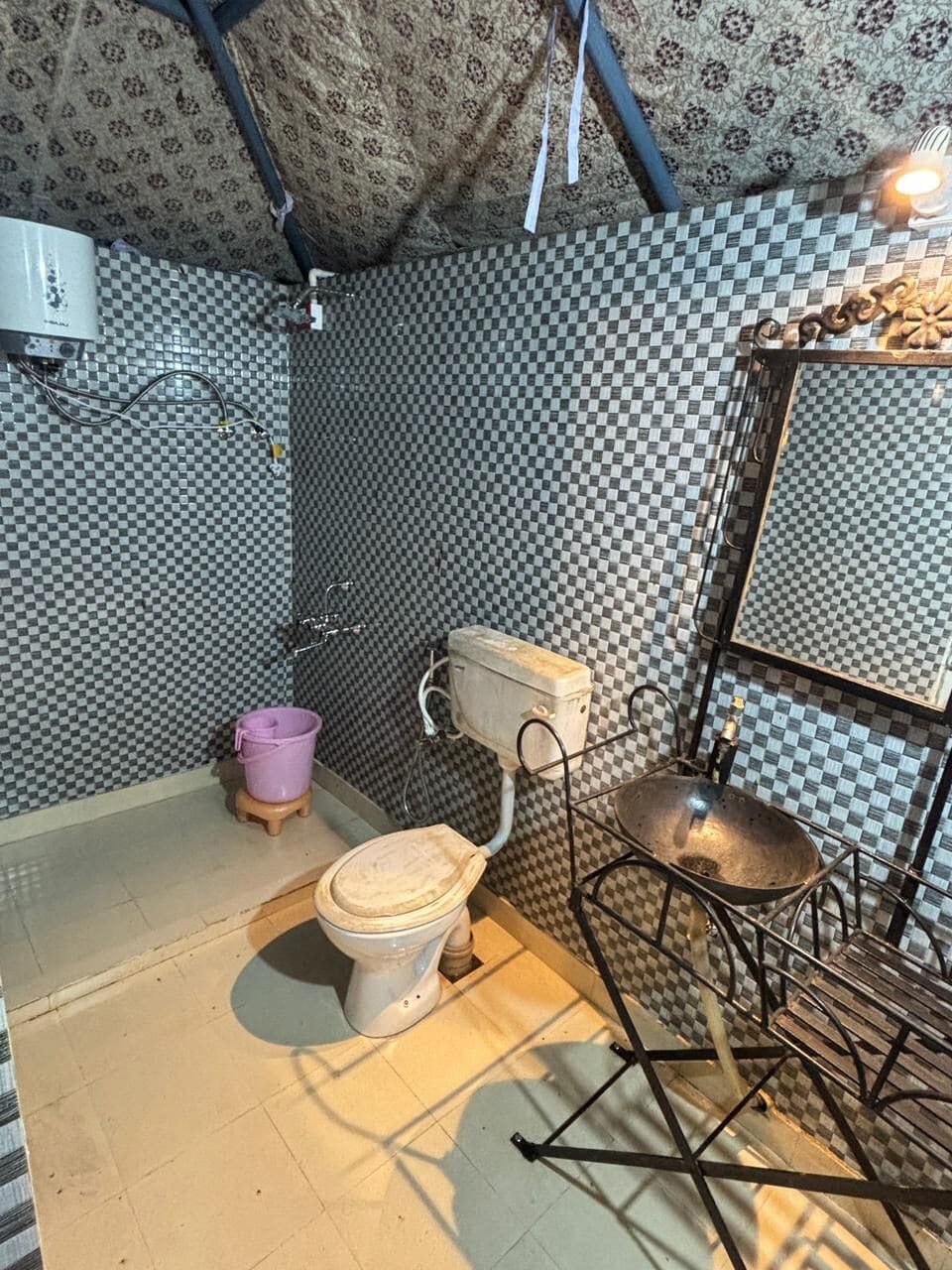 A bathroom with a toilet, a bucket, a metal rack, and a patterned wall.