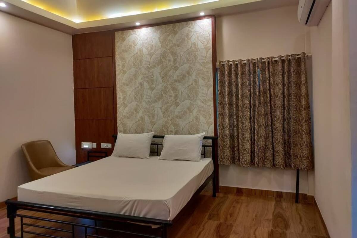 Une chambre à coucher avec un lit, une chaise, un climatiseur fixé au mur et un rideau à motifs.