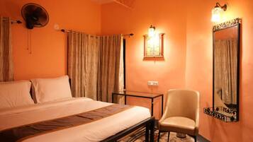 Habitación de hotel con una cama, una silla, una mesa, cortinas, un ventilador de pared y una lámpara de pared.