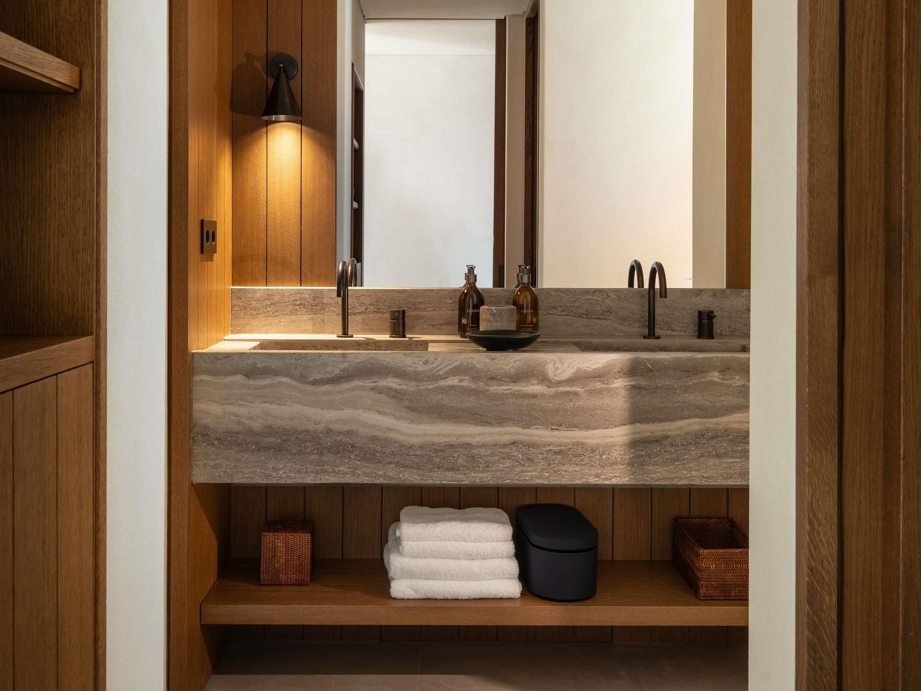 Une salle de bain avec un meuble-lavabo en bois, un évier doté d’un plan de travail en marbre et un miroir.