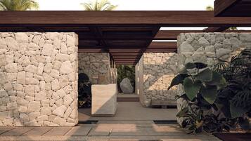 Une structure en pierre avec une pergola en bois, un bloc de béton et des plantes tropicales.