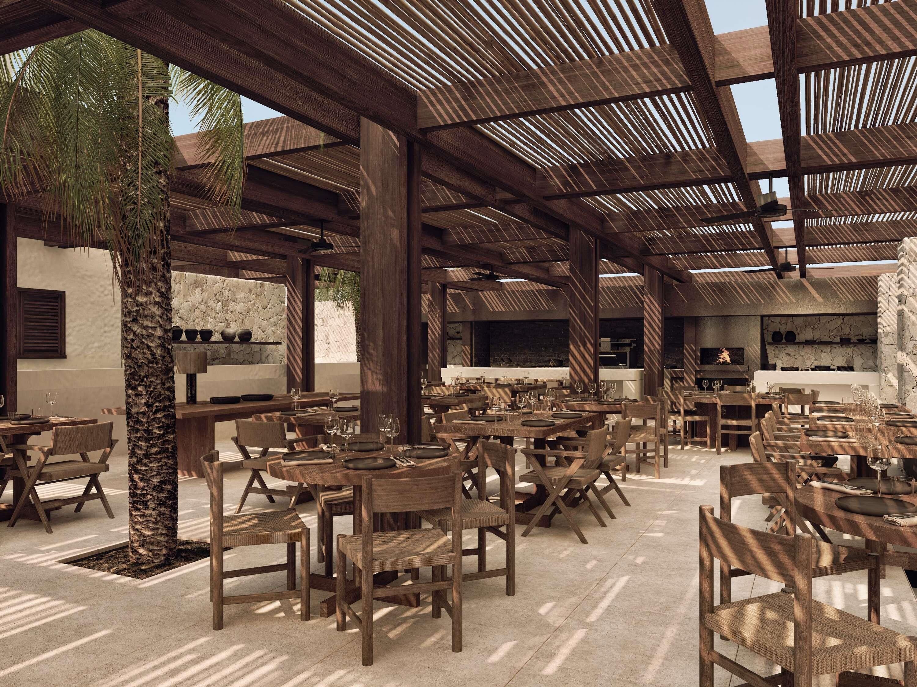 Un espace extérieur aménagé pour les repas, avec des tables et des chaises en bois, un mur en pierre et un grand arbre.